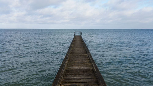 View of pier over calm sea against cloudy sky