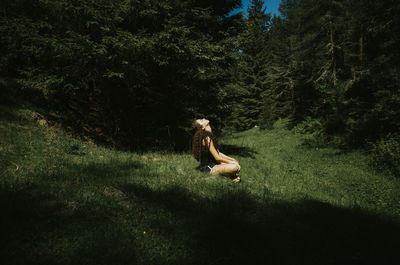 Side view of young woman sitting on grassy field during sunny day