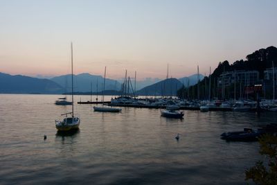 Boats moored in harbor at sunset