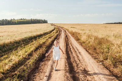 Full length of girl running on dirt road against sky