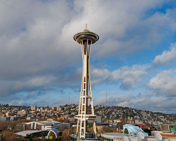 Tower amidst buildings in city against cloudy sky