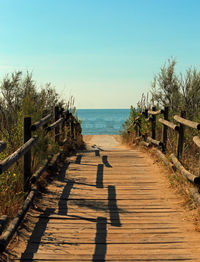 Wooden post on footpath by sea against clear sky