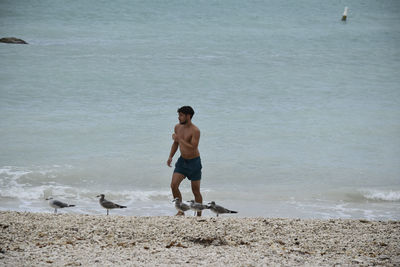 Rear view of shirtless man standing on beach