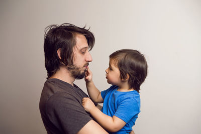 Father in the gray shirt holding a son in a blue t-shirt in the hands of a white wall