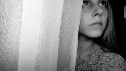 Close-up of thoughtful girl standing by curtain