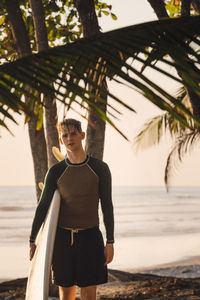 Portrait of confident young man carrying surfboard at beach