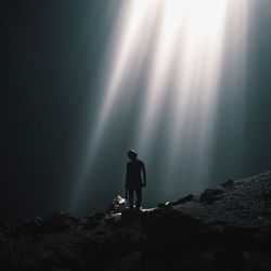 Silhouette person standing under sunbeam in goa jomblang cave