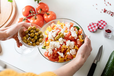 Healthy eating. female hands making greek salad adding olives to the bowl