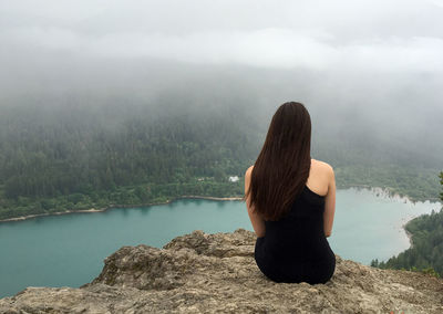 Rear view of woman sitting on mountain against lake