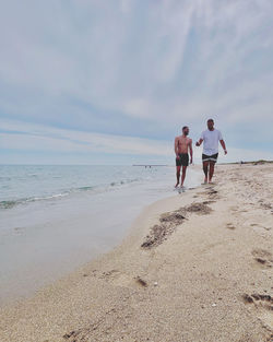 Rear view of people walking on beach against sky