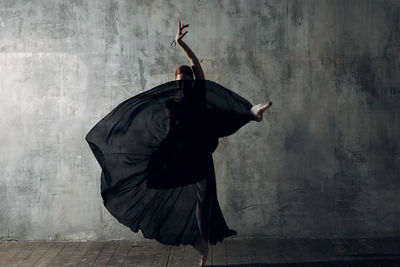 Woman dancing against gray wall