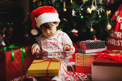 Cute girl opening christmas present against tree at home