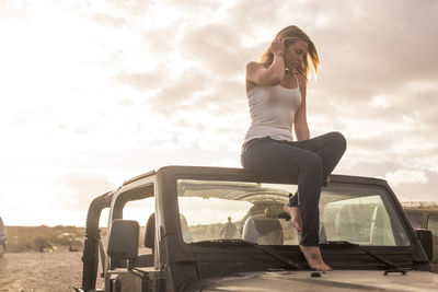 Full length of young woman sitting on off-road vehicle against sky during sunset
