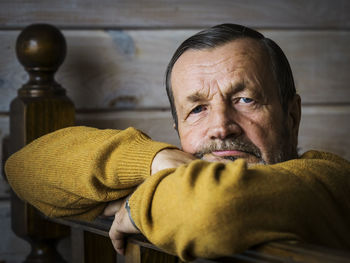 Portrait of senior man wearing sweater leaning on wooden railing while sitting at home