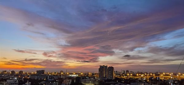 Illuminated buildings in city against sky during sunset