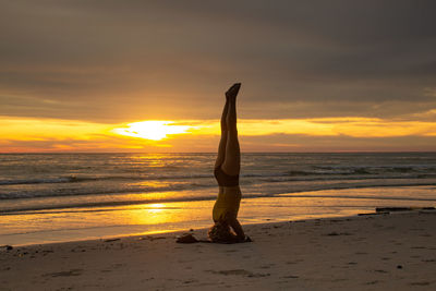 Woman standing on beach against sky during sunset