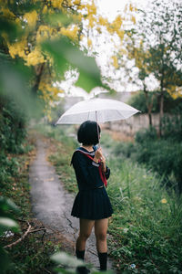 Full length of woman standing on tree during rainy season