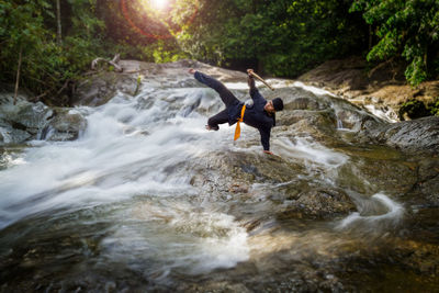 Man practicing handstand in river at forest