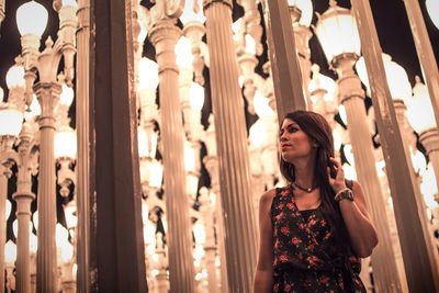 Low angle view of young woman looking away while standing by illuminated columns at night