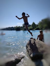 Man jumping on rock by sea against sky