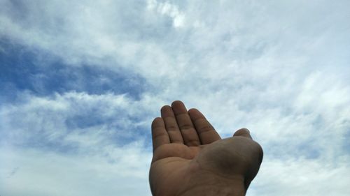 Cropped hand reaching cloudy sky