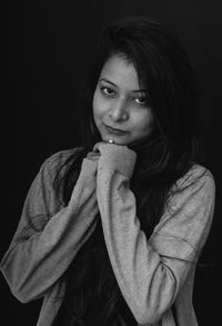 Portrait of beautiful young woman standing against black background