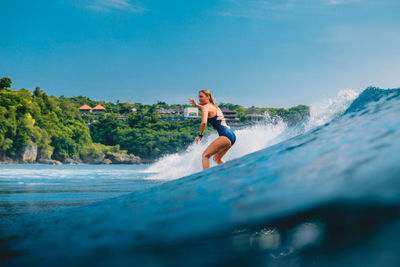 Full length of young woman surfing in sea against sky