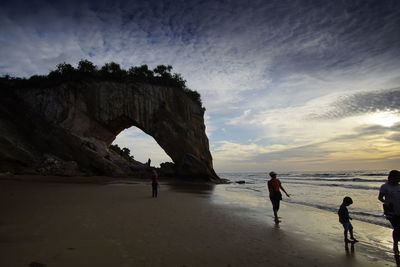 People on rocks at beach against sky