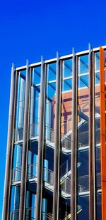 Low angle view of glass building against clear blue sky