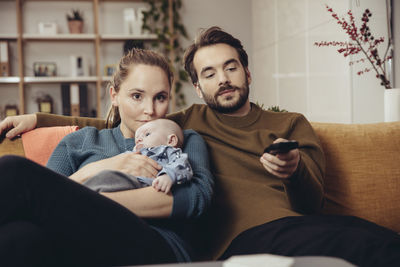 Father and mother sitting with baby on couch watching tv
