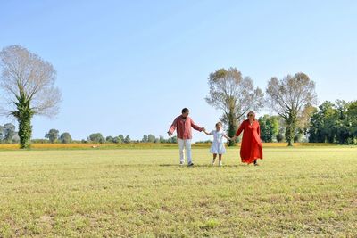Family walking on field against clear sky