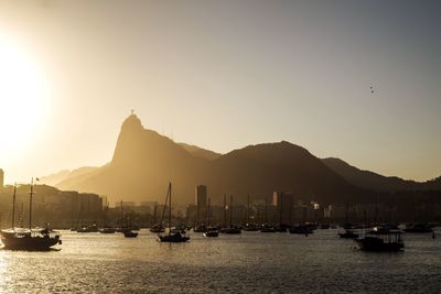 Boats on sea by silhouette mountains against clear sky