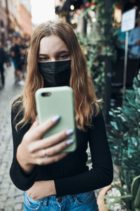 Girl wearing mask holding smart phone outdoors