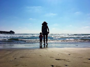 Rear view of friends standing on beach against sky