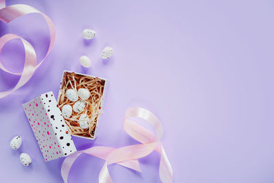 Easter creative layout with easter eggs in a gift box with pink ribbons on purple background