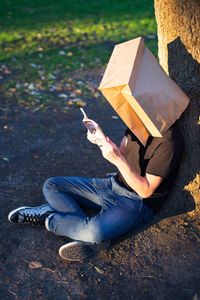 High angle view of man wearing paper bag while reading book outdoors