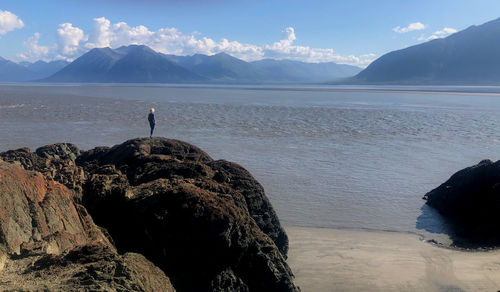 Woman standing on rock by mountains against sky