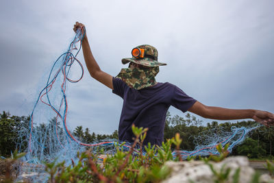 Fisherman holding fishing net on field against sky