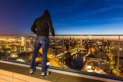 Rear view of man looking at illuminated city buildings
