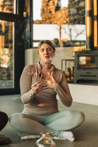 Woman with hand on chest holding burning sandalwood while meditating at retreat center