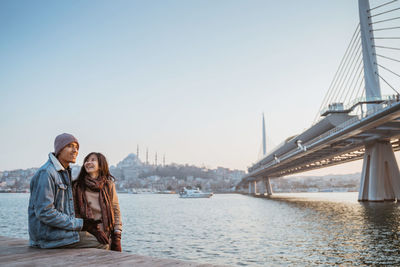 Portrait of smiling woman standing against river against clear sky