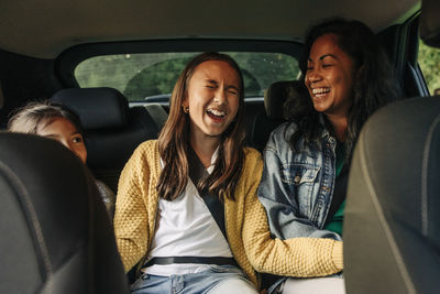 Girl laughing while sitting with mother and sister in car during road trip