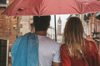 Rear view of couple standing with umbrella in city