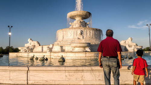 Rear view of father and son standing against fountain
