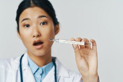 Portrait of doctor holding thermometer against gray background