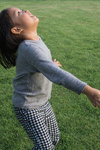 Side view of girl looking up while standing on field