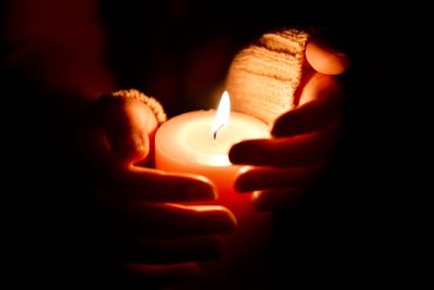 Cropped image of hands covering lit candle in darkroom