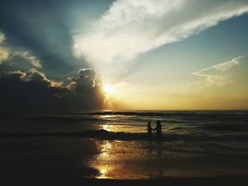 Silhouette people on beach against sky during sunset