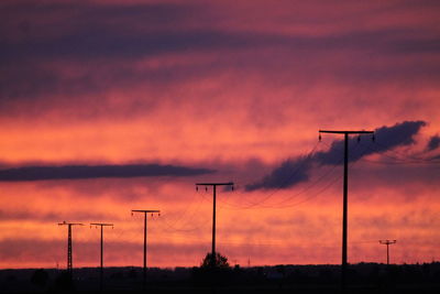 Silhouette electricity pylon on field against orange sky