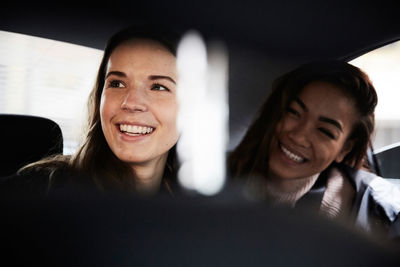 Smiling young female friends looking away while sitting in taxi